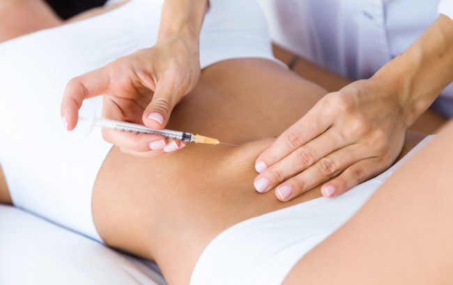 Portrait of surgeon making injection into female body. Liposuction concept.